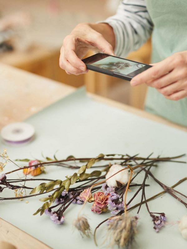 Closeup of unrecognizable woman taking mobile photo of flower composition in art studio, copy space